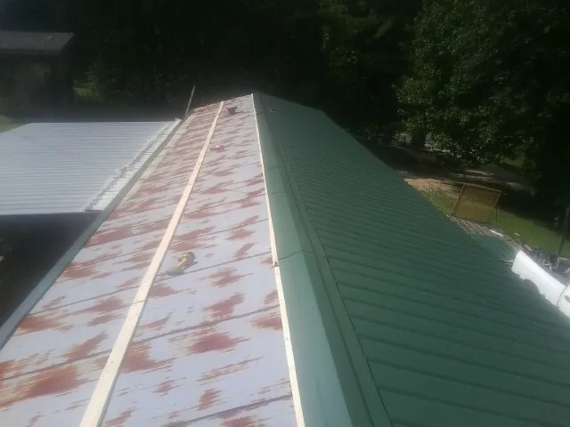 Old rusted panels beside newly installed green metal roofing — Wind Damage Roof Repair by Roofing Brothers in Whiteville
