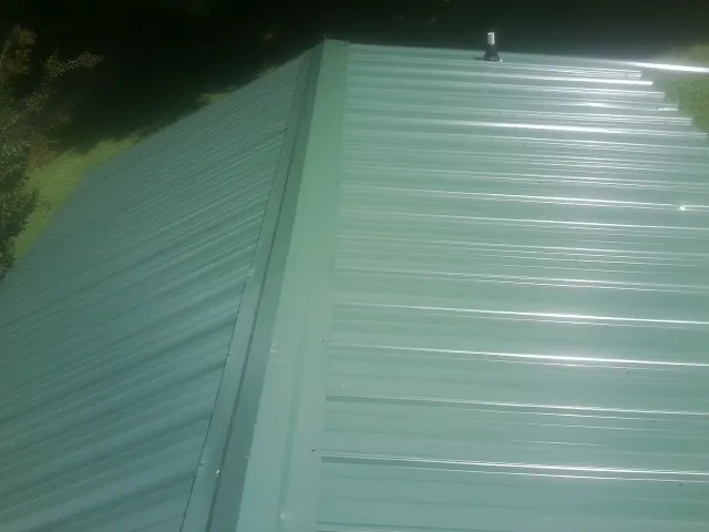New green metal panels meeting at the ridge of a roof — Flat Roof Repair work by our crew in Whiteville