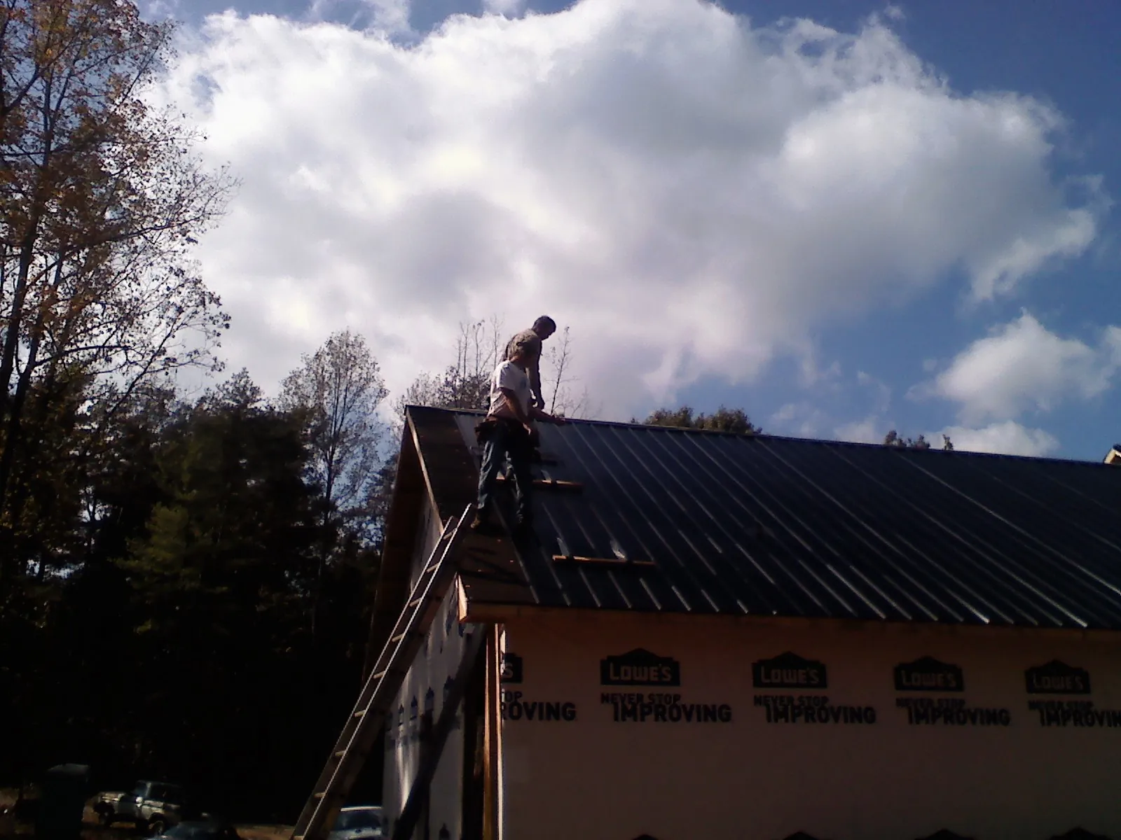 Roofer fastening dark metal panels high against a cloudy sky, from a Roof Inspection job in Whiteville