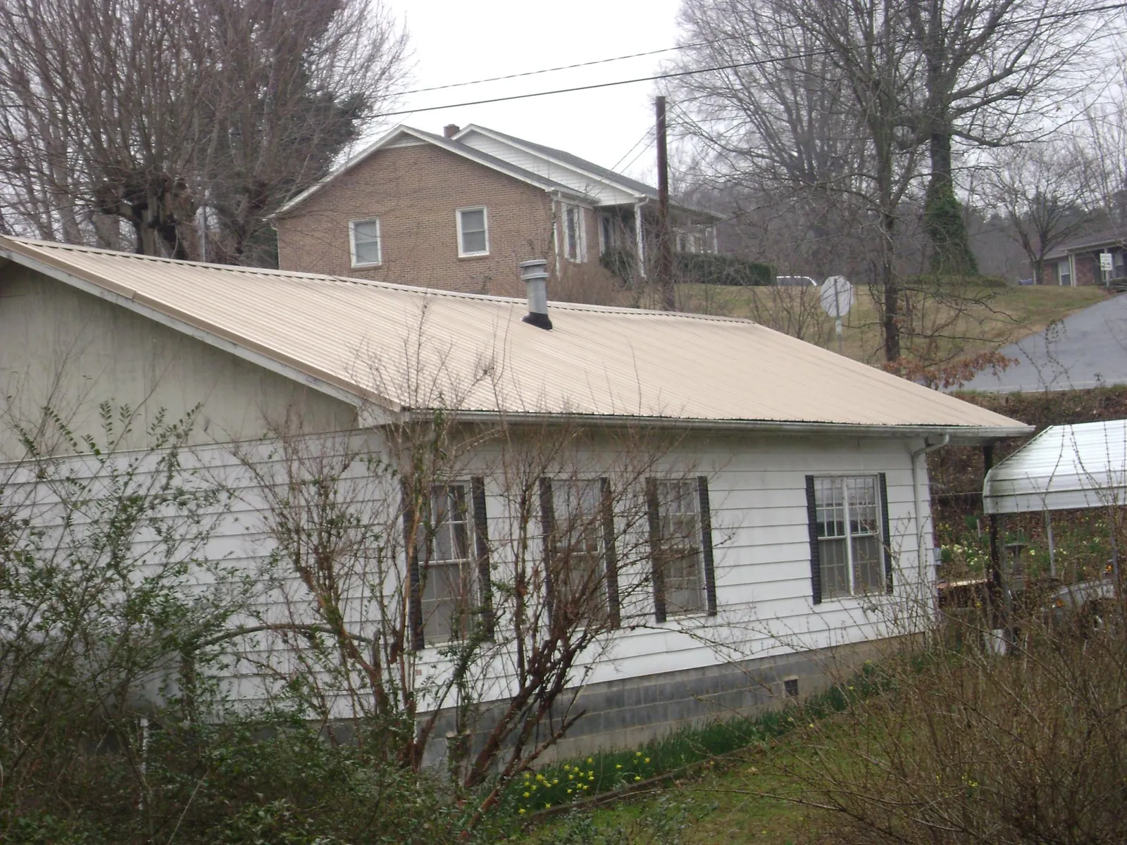 Tan metal roof on a white sided house set into a hillside — Commercial Roofing by Roofing Brothers in Whiteville
